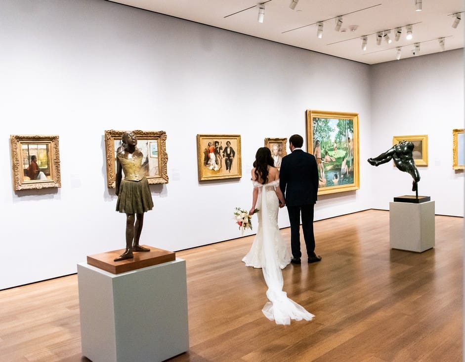 Bride and groom standing holding hands looking at the art exhibits with Degas bronze dancer in full ground at Harvard Art Museum