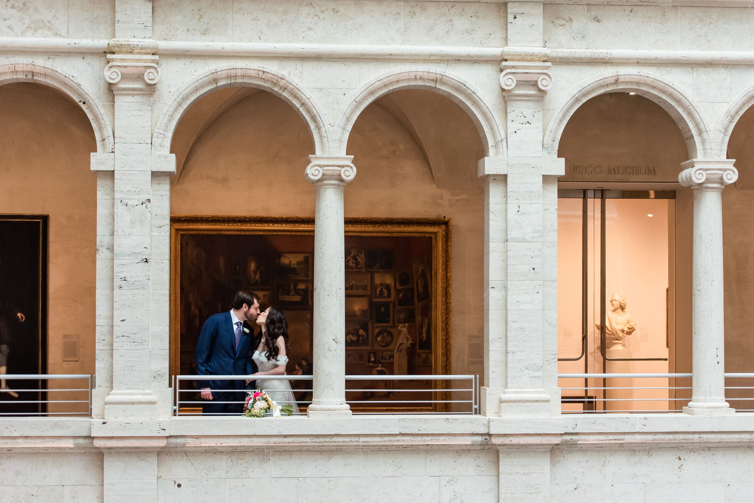 Bride & groom kiss on balcony between arches at Harvard Art Museum
